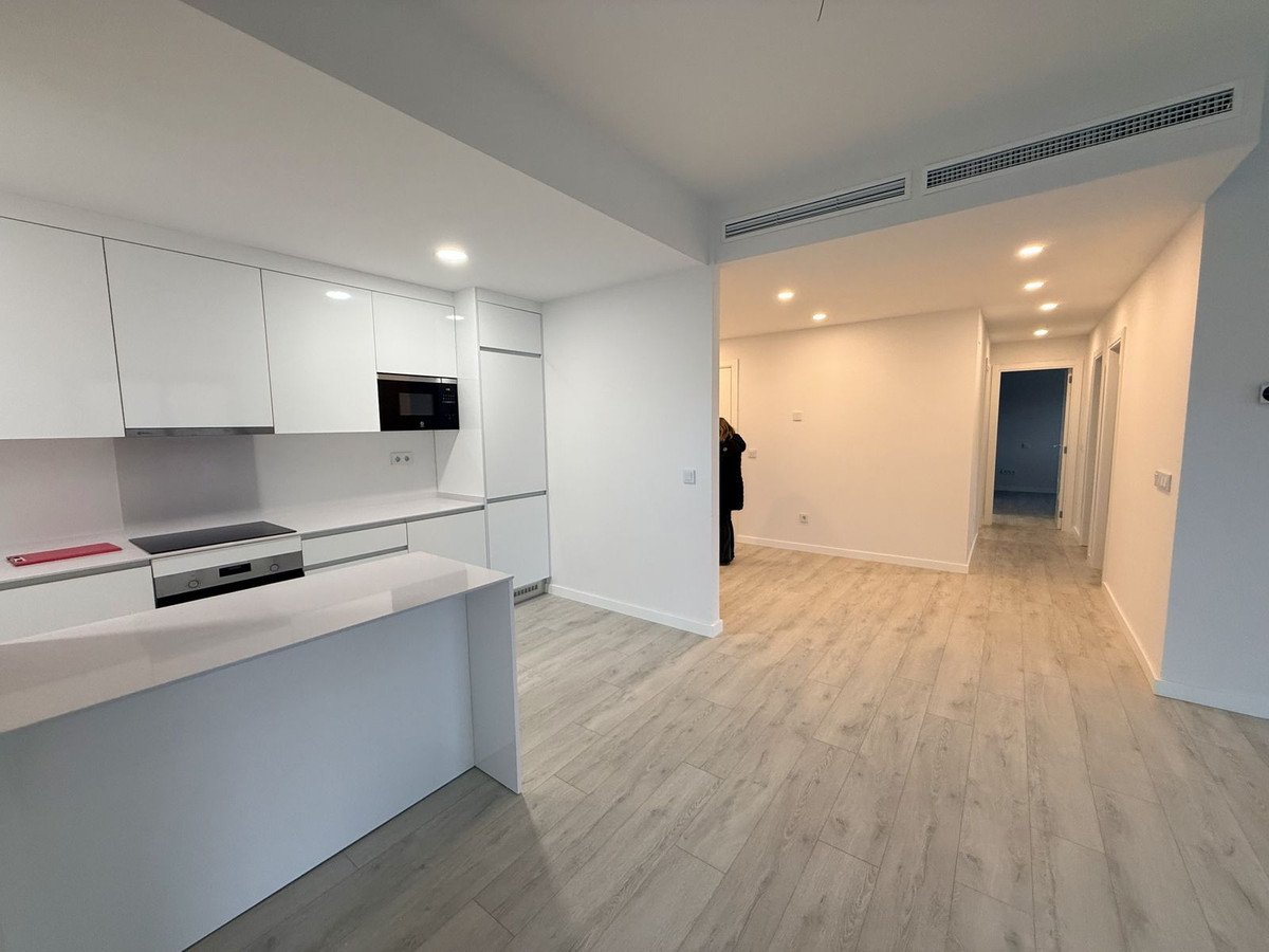 Modern kitchen with white cabinets, island, and light wood flooring in an open-plan apartment.
