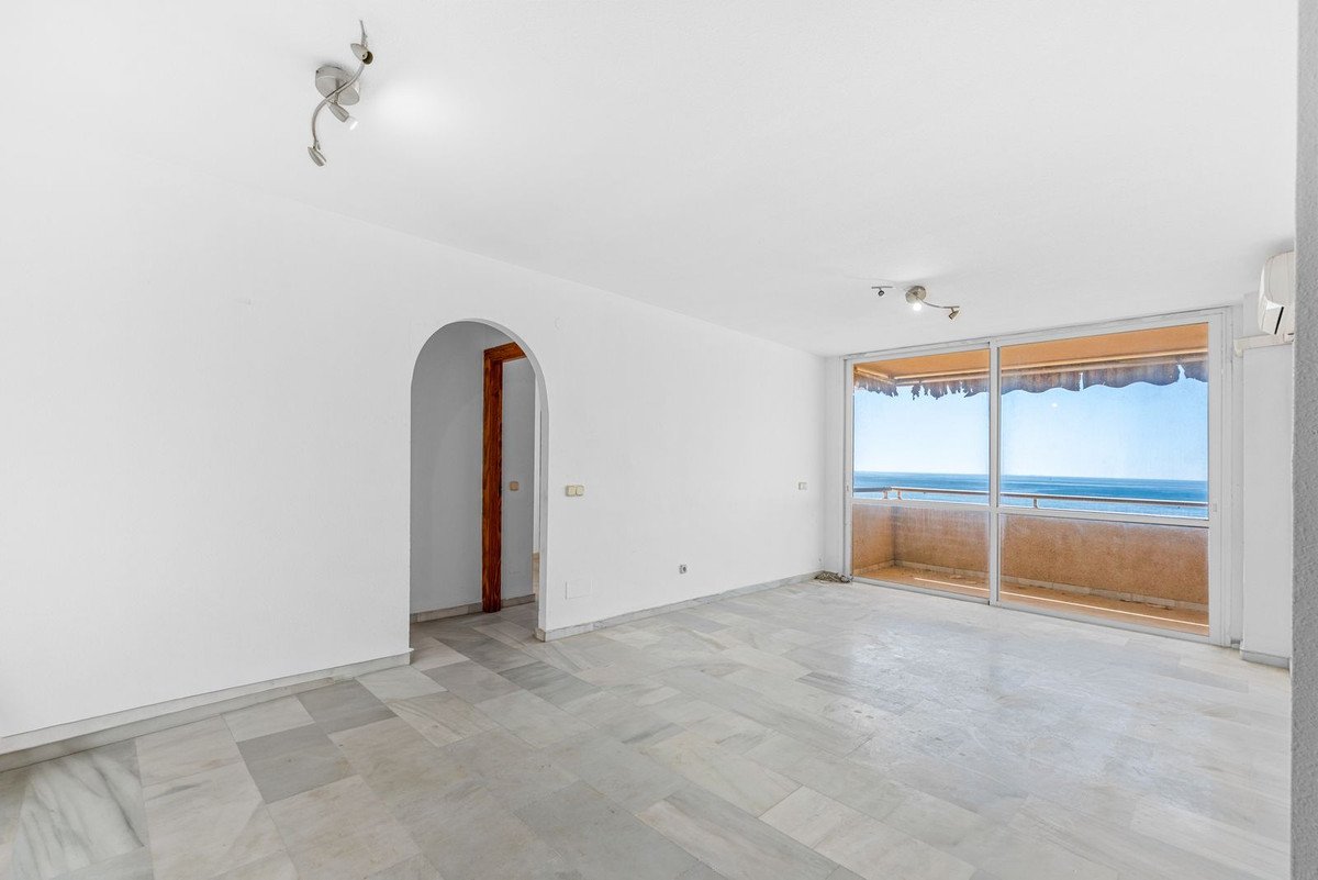 Empty room with white walls and marble flooring, featuring large glass doors leading to a balcony with ocean view