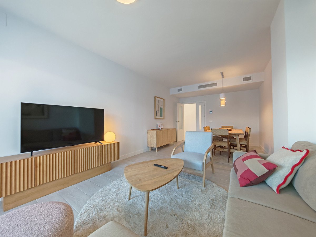 Modern living and dining area with a large TV, comfortable sofa, light wood furniture, and stylish accent pillows.