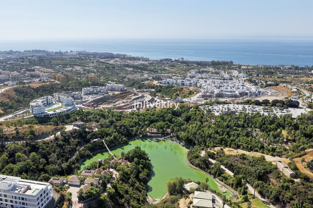An aerial view of a resort estate with a green lake, surrounded by lush trees and offering a distant view of the sea.