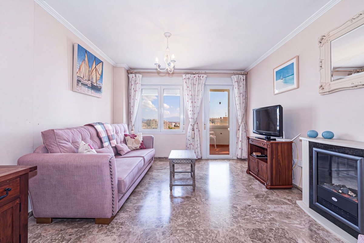 A living room with a pink sofa, television, fireplace, and balcony with a view of the town and sky.