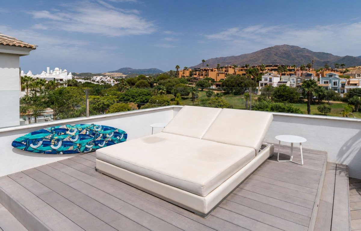 Rooftop terrace with lounge bed, surfboard, and panoramic view of mountains and resort.
