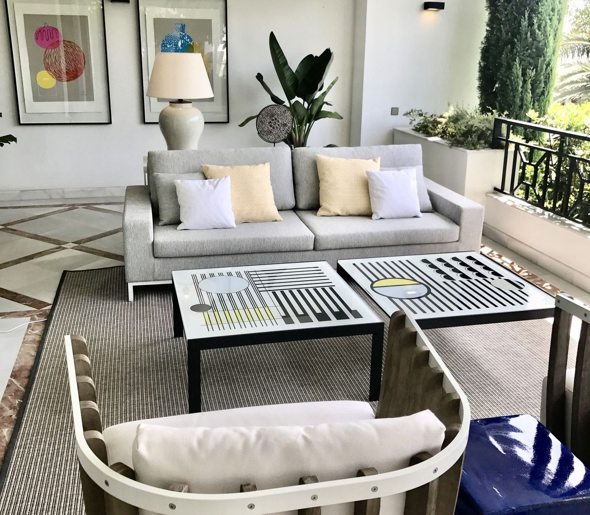 Modern living room featuring a grey sofa with beige and white pillows, abstract coffee tables, and a large indoor plant