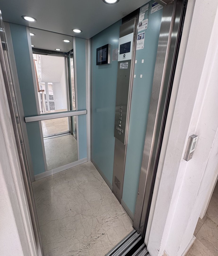 Modern elevator interior with light blue walls, stainless steel panel, floor display showing '2', and marble floor.
