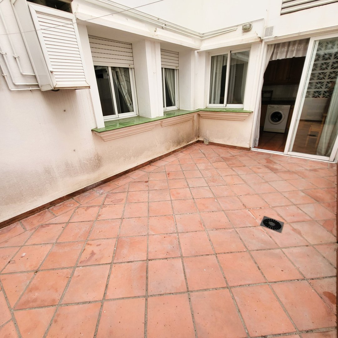 Tiled outdoor terrace with windows and sliding glass doors leading to an interior space with a washing machine.