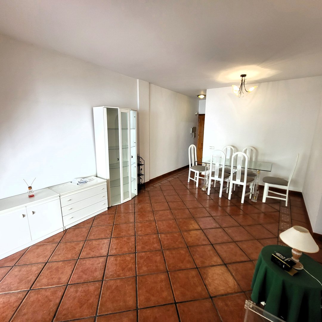 Spacious living and dining area with terracotta tiled floors, glass-top dining table, chairs, and white cabinets with display case.