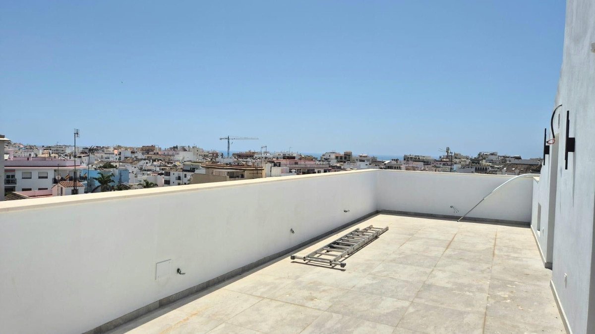 A spacious rooftop terrace with a city view and the sea in the distance, featuring white walls and tiled flooring.