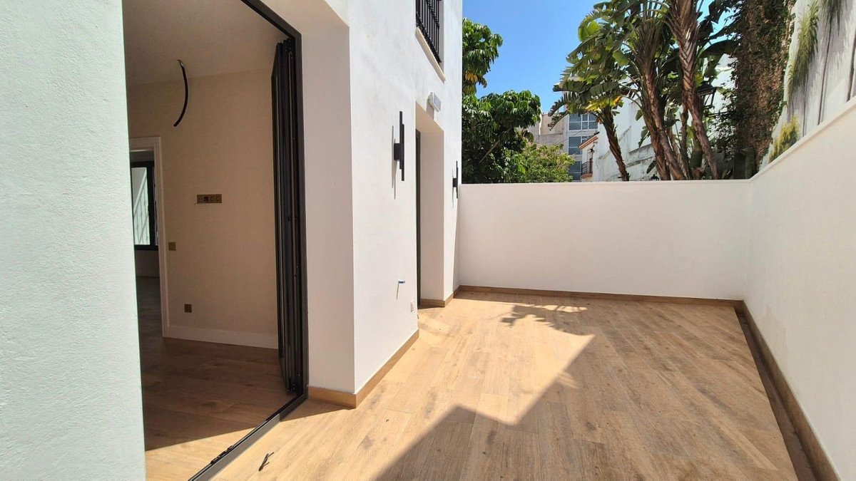 Modern terrace with light wood flooring, featuring black wall lights and lush green trees visible in the background.