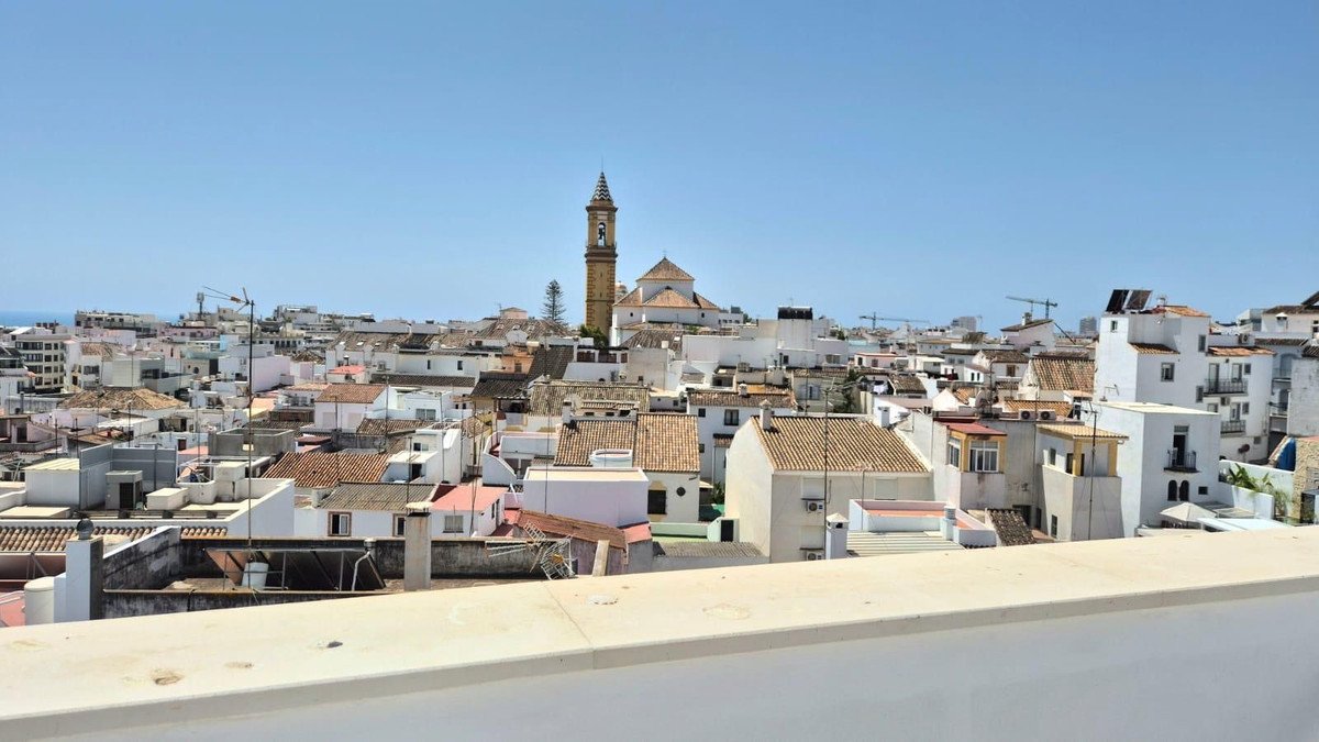 Panoramic view of a white Spanish town with terracotta roofs and a church tower under a clear blue sky.
