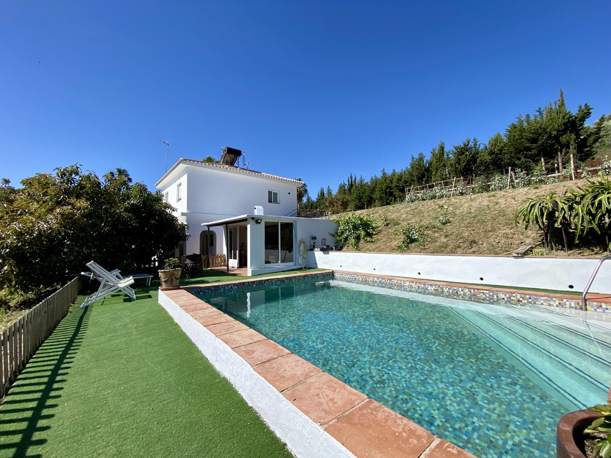Villa with private pool, green lawn, and mountain views under clear blue sky.