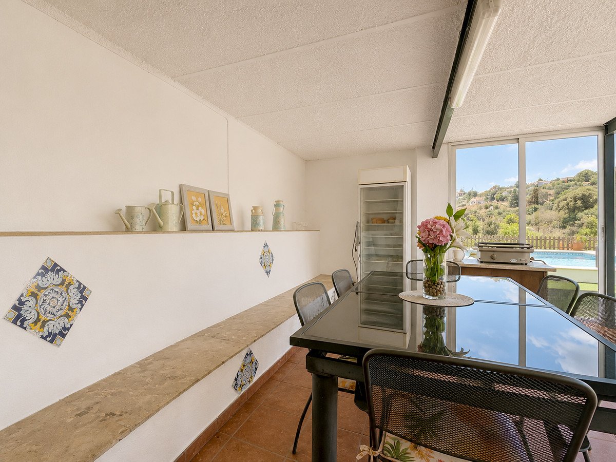 Dining room with large window overlooking a swimming pool and hilly landscape