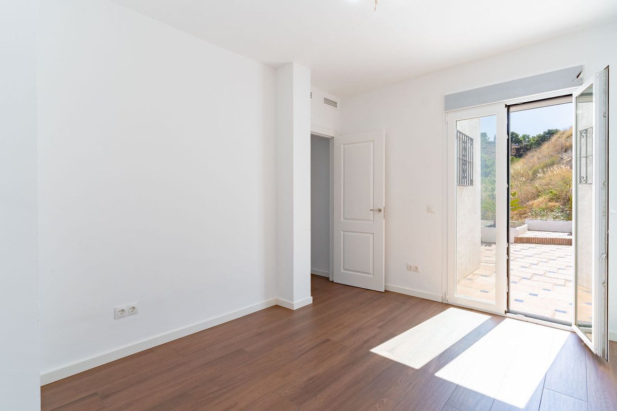 Empty room with wooden floor, white walls, and a sunlit floor leading to a garden view