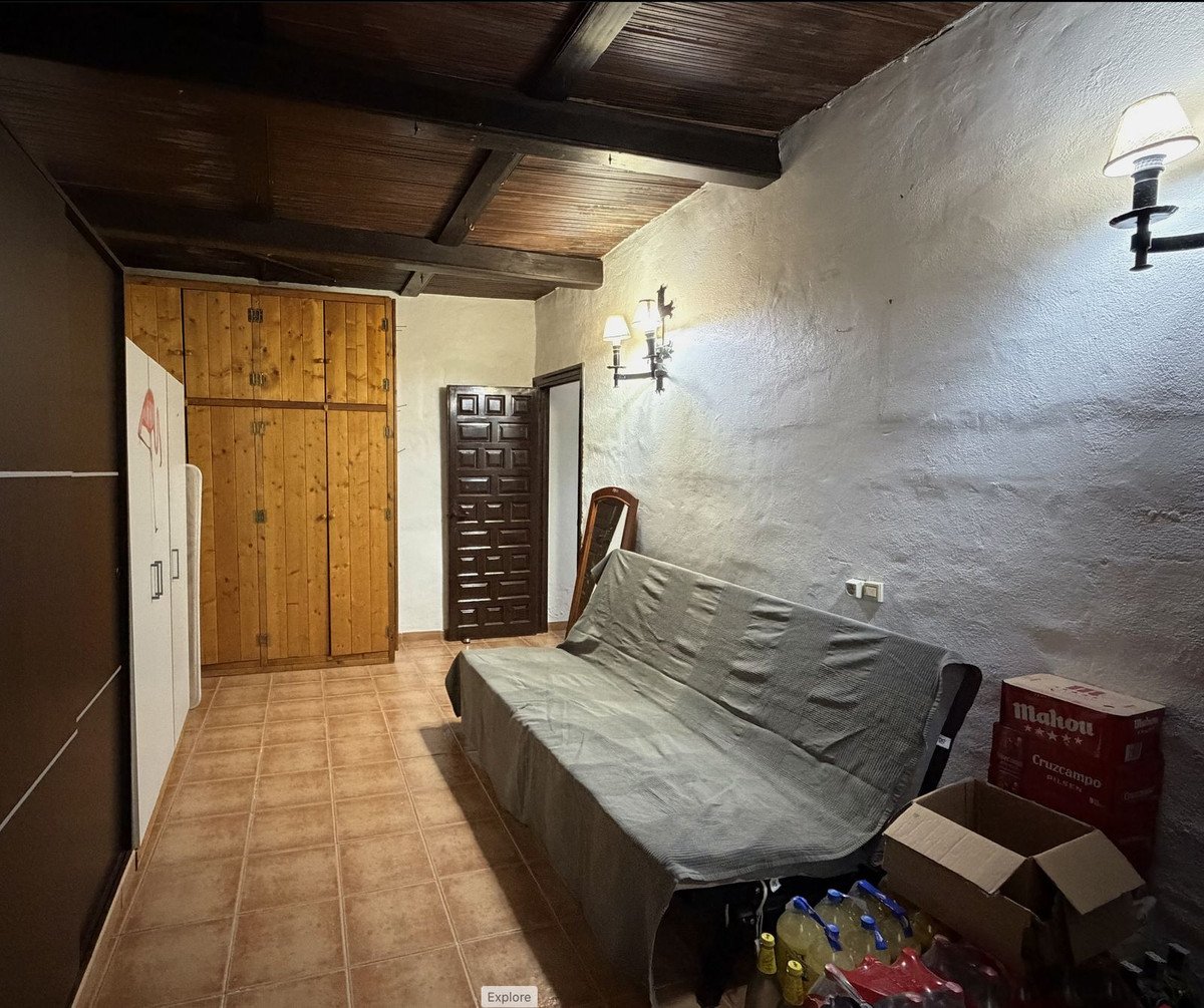 A cozy room with wooden ceiling beams, tiled floor, and a covered sofa near a wooden wardrobe.