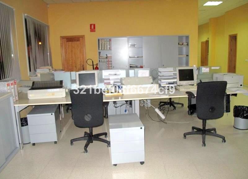 An office space with multiple workstations, computers, printers, and chairs. Features filing cabinets and storage units.