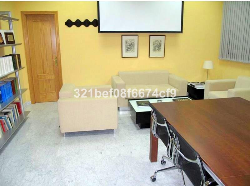 A modern conference room with beige sofas, a wooden desk, a projector screen, and artwork on a yellow wall.