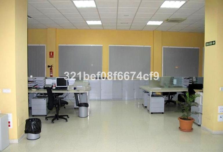 Modern office space with multiple desks, computers, chairs, and filing cabinets under fluorescent lighting.