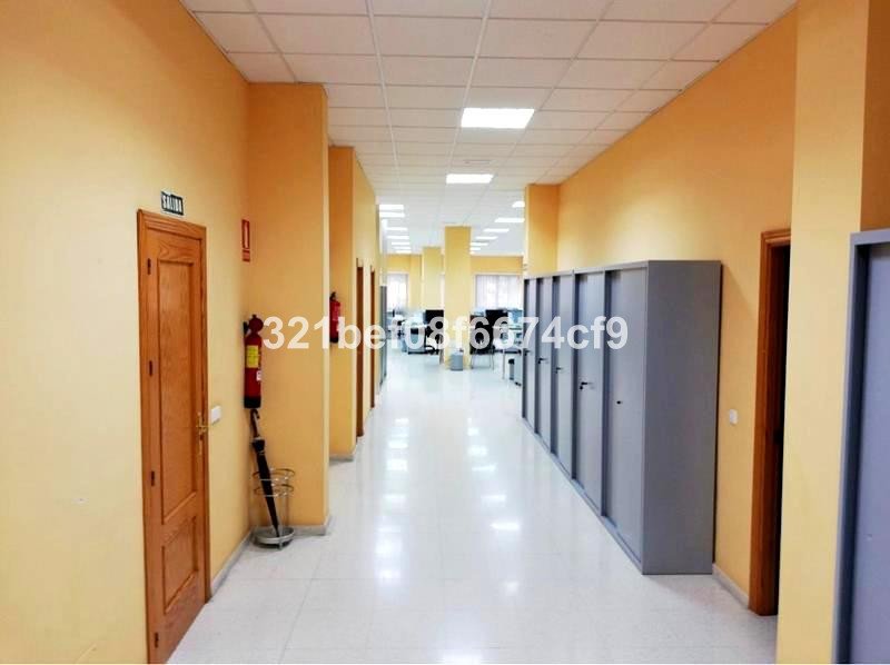 A long office hallway with yellow walls, doors, cabinets, and fluorescent lighting.