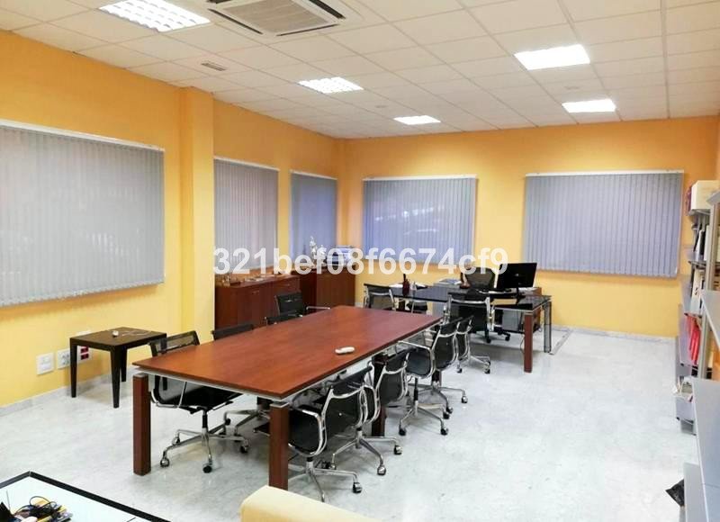 Modern conference room with a large wooden table, chairs, and workstations. Brightly lit with natural light from large windows.