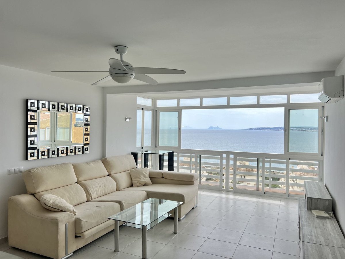 Modern living room with beige sofa, glass coffee table, and large windows overlooking the sea