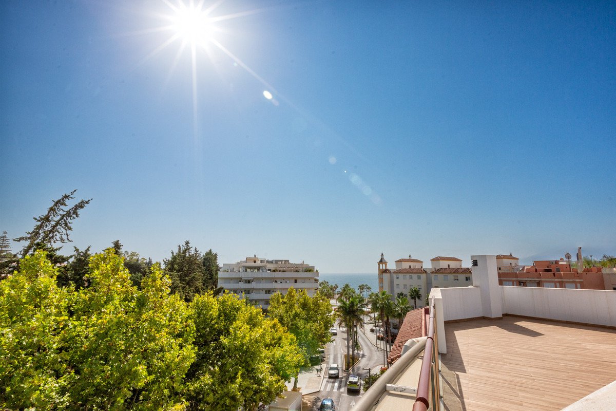 Sunlit balcony view of coastal town with palm trees, sea, and clear blue sky.
