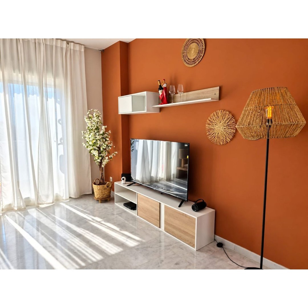 Modern living room with a TV stand, plant, and large window with white curtains.
