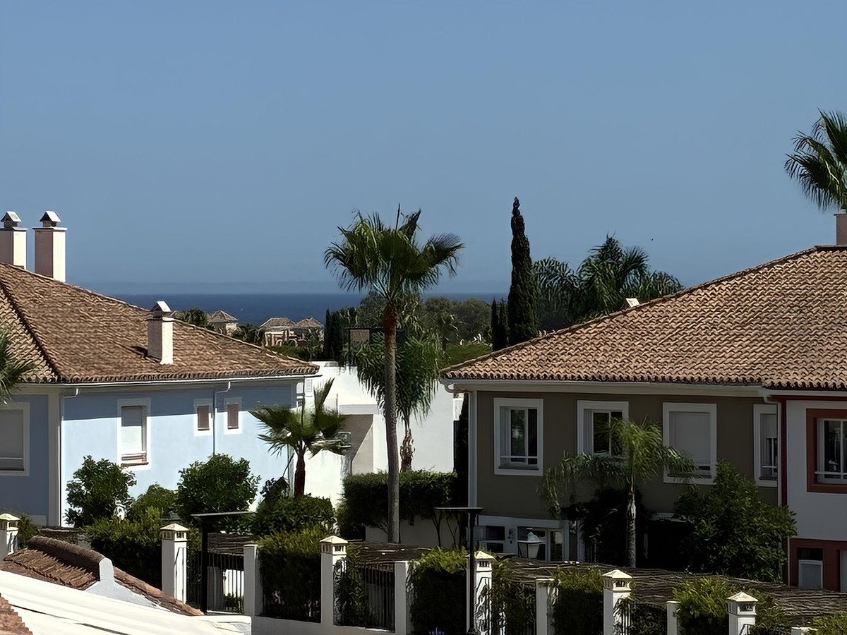 Houses with tiled roofs and palm trees with a distant view of the ocean under a clear blue sky.