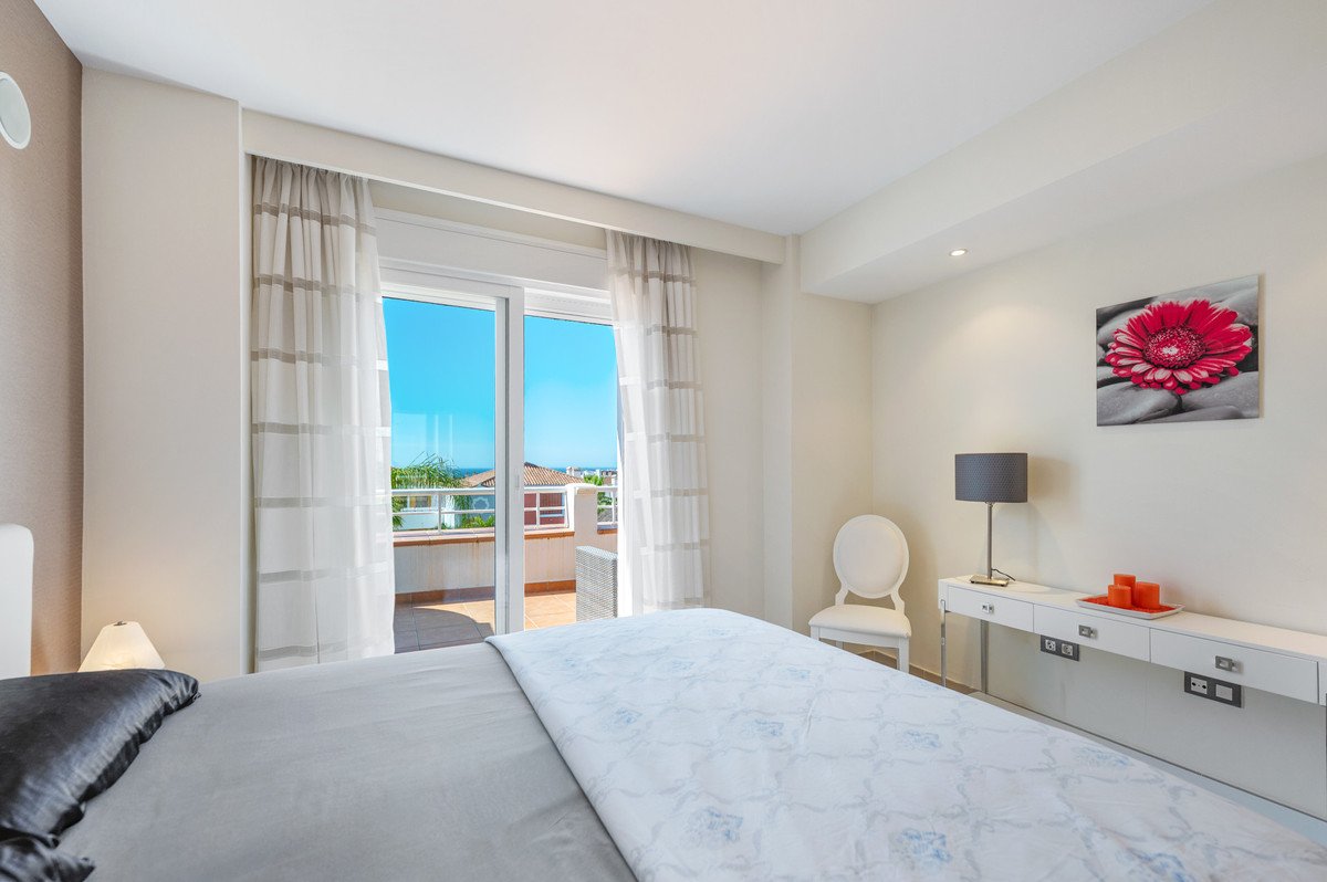Modern bedroom with ocean view, balcony access, white furniture, and red floral artwork.