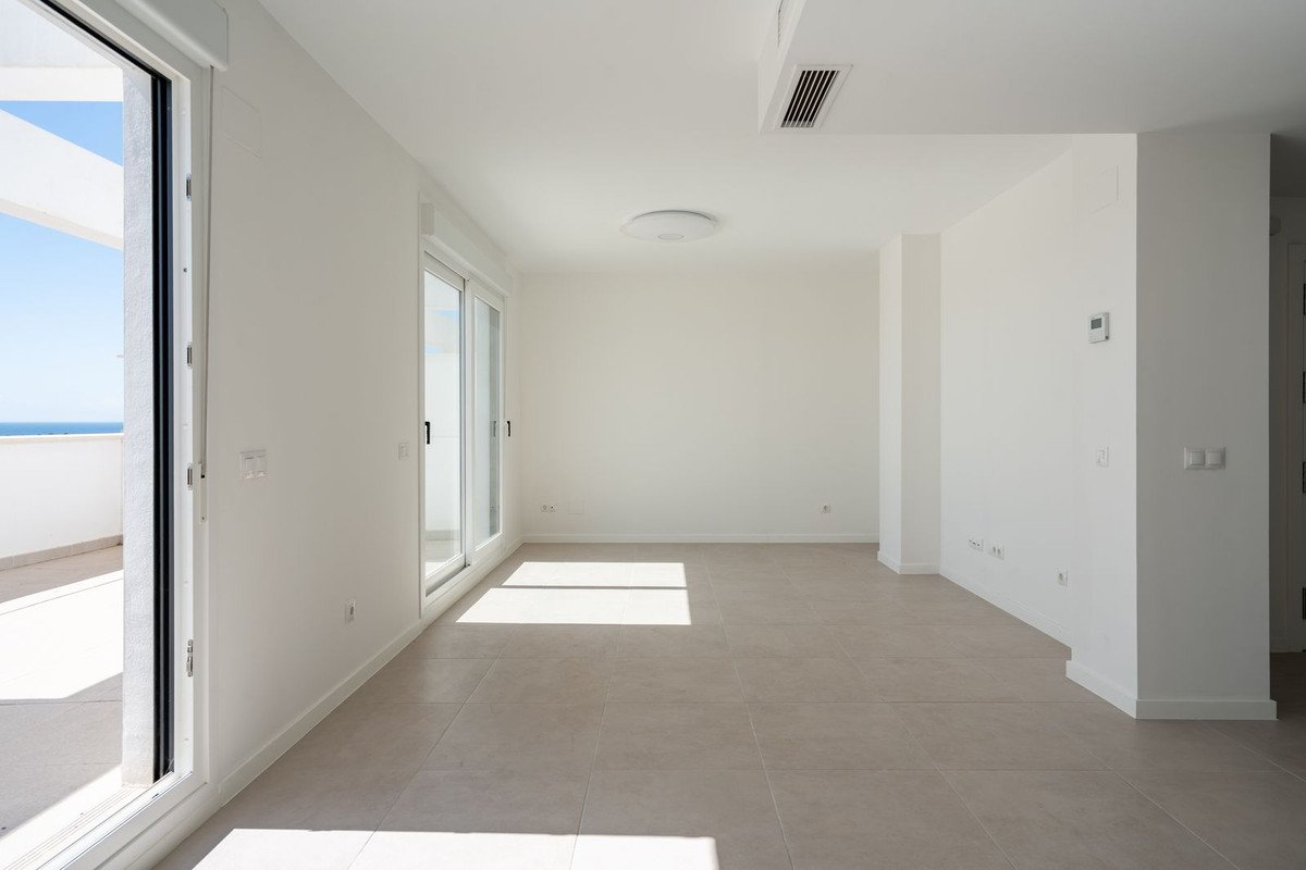 Spacious living room with sliding glass doors opening to a balcony with a sea view. Modern interior with tiled floors.