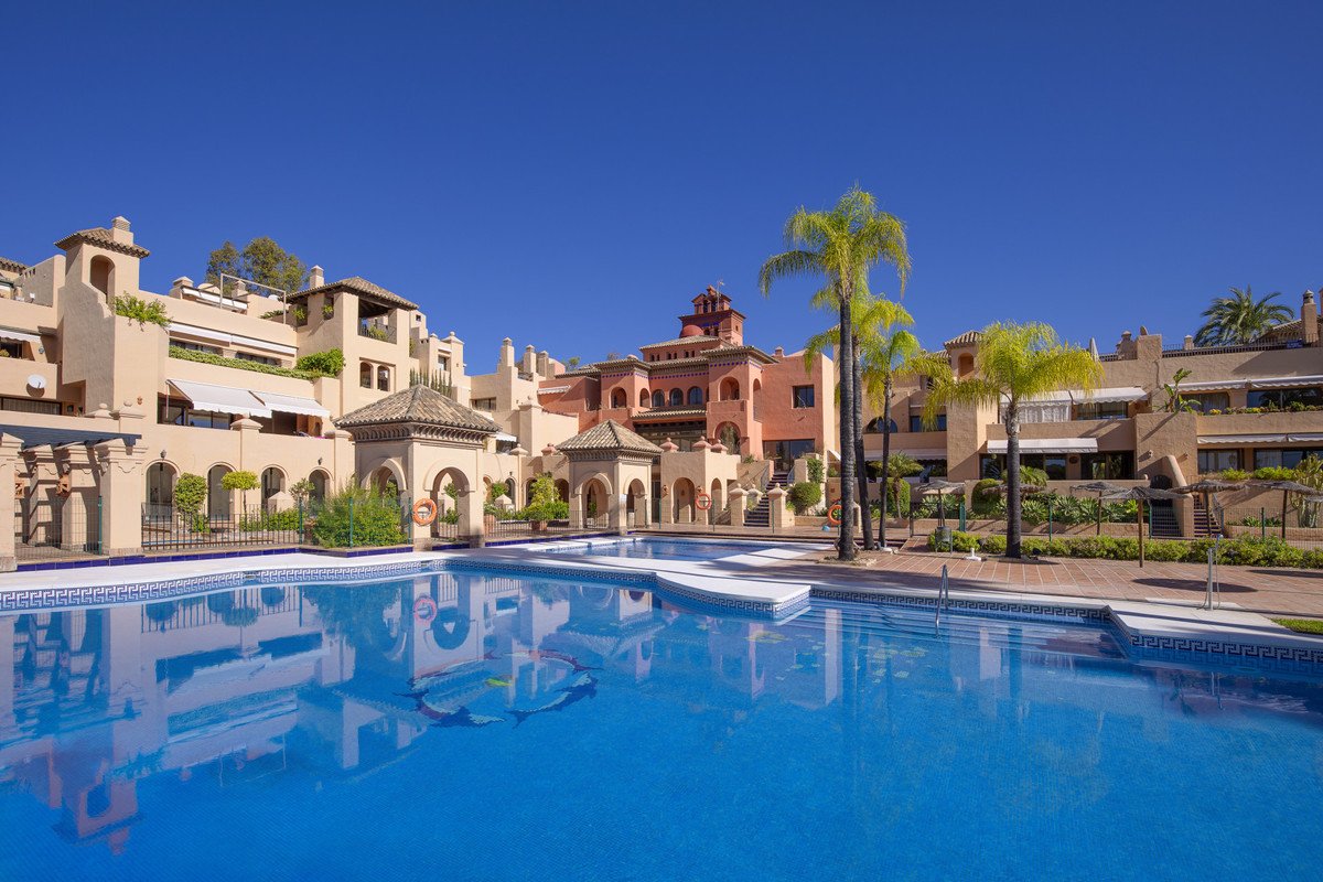 Luxurious pool area with Mediterranean-style houses and palm trees under a clear blue sky