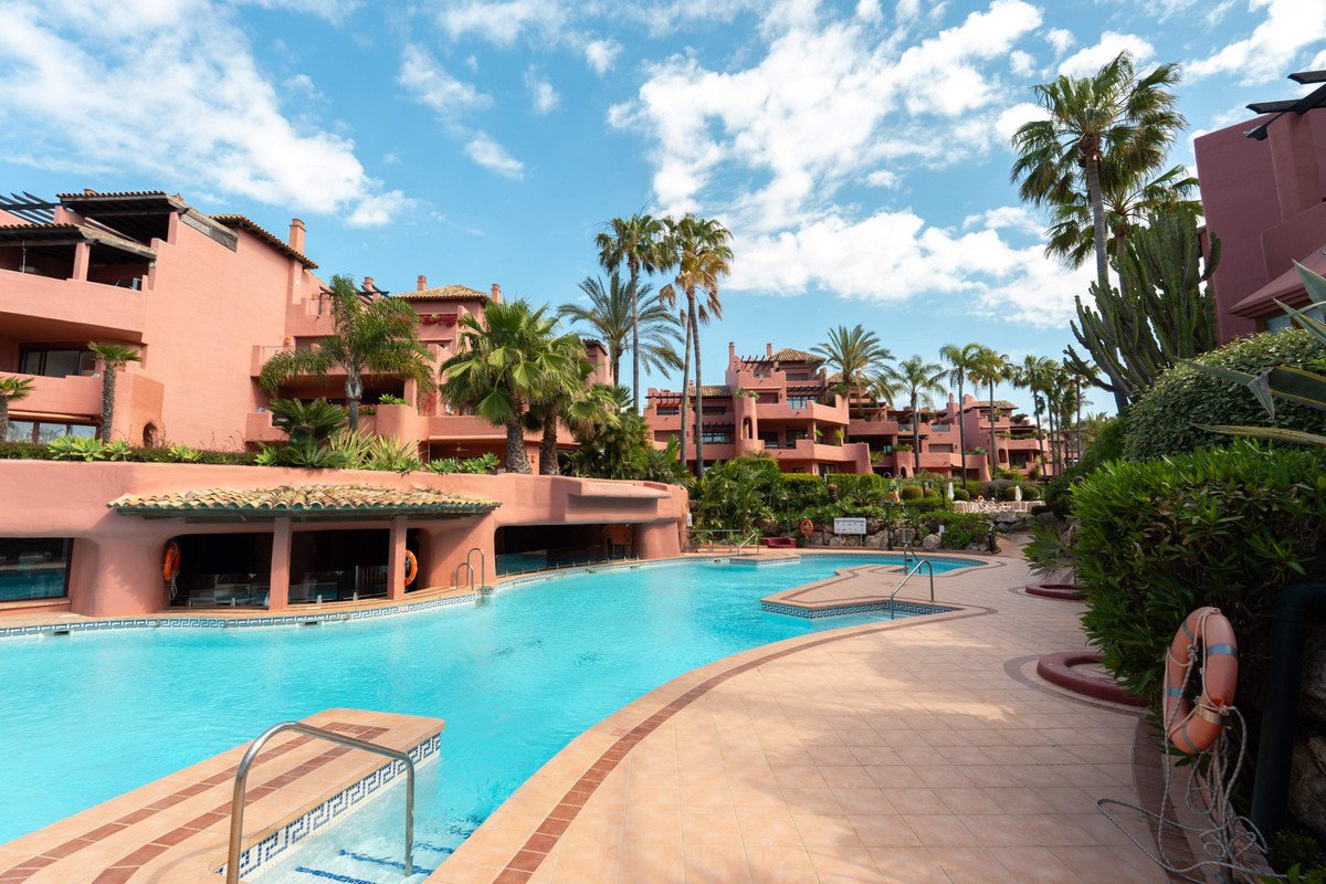 Villa with pool, palm trees, and terracotta buildings under a blue sky.