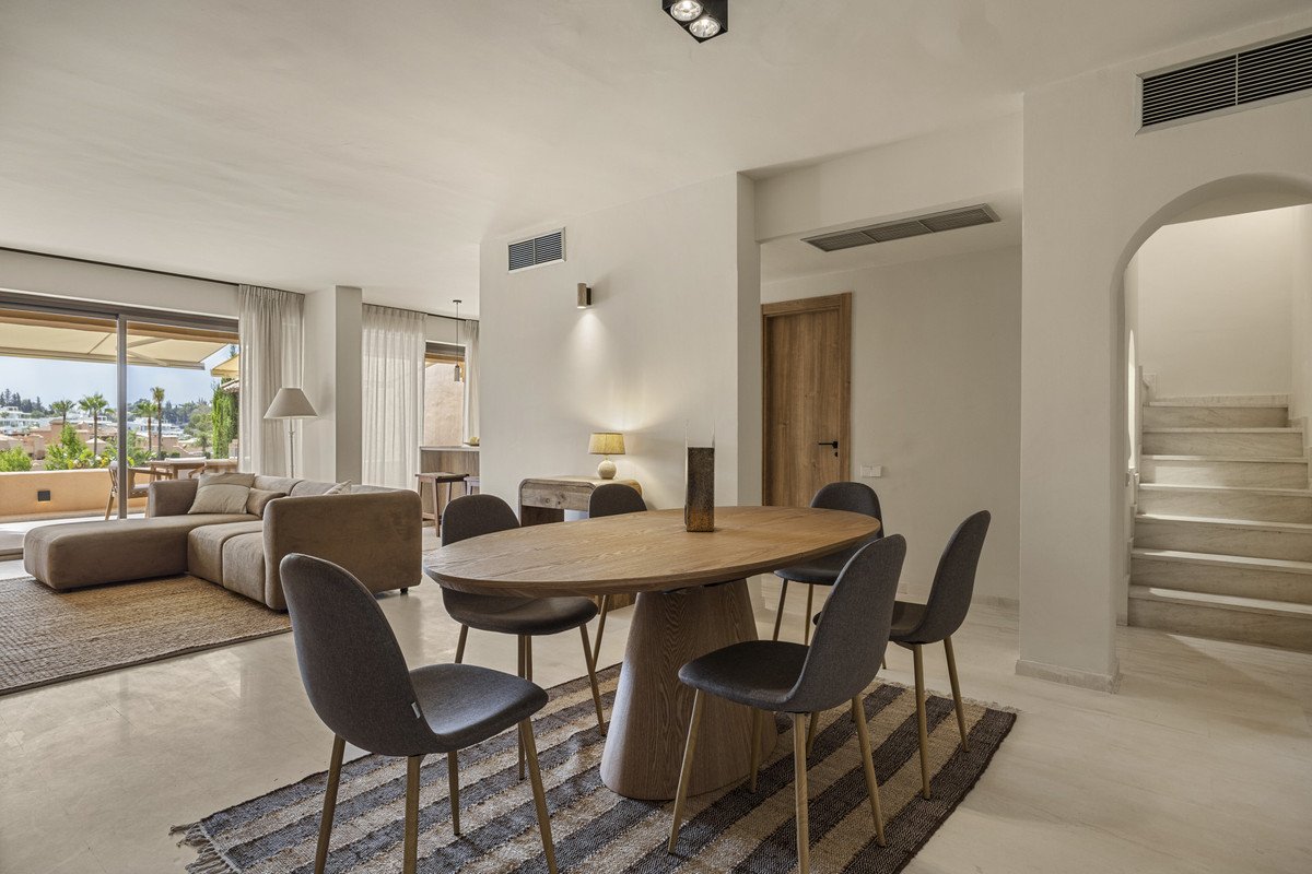 Modern living room with large wooden table, grey chairs, and a beige sofa overlooking a balcony
