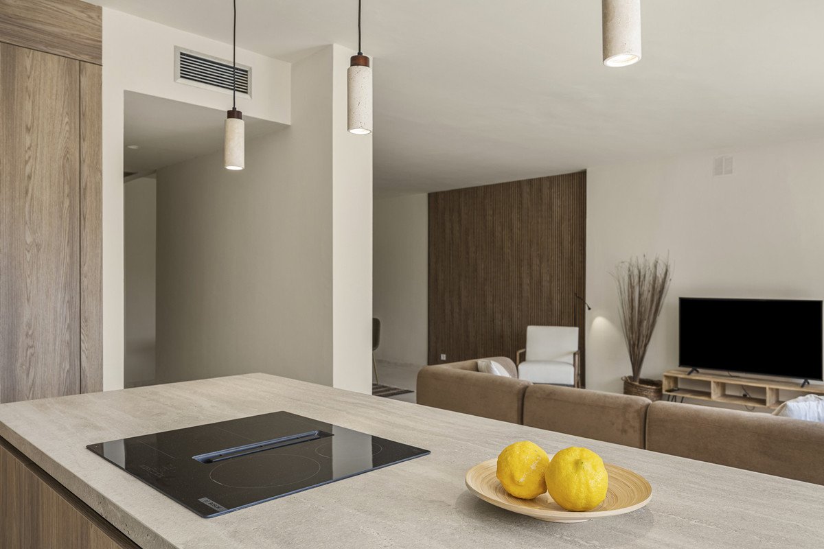 Modern living room with beige sofa, flat-screen TV, and kitchen island with lemons