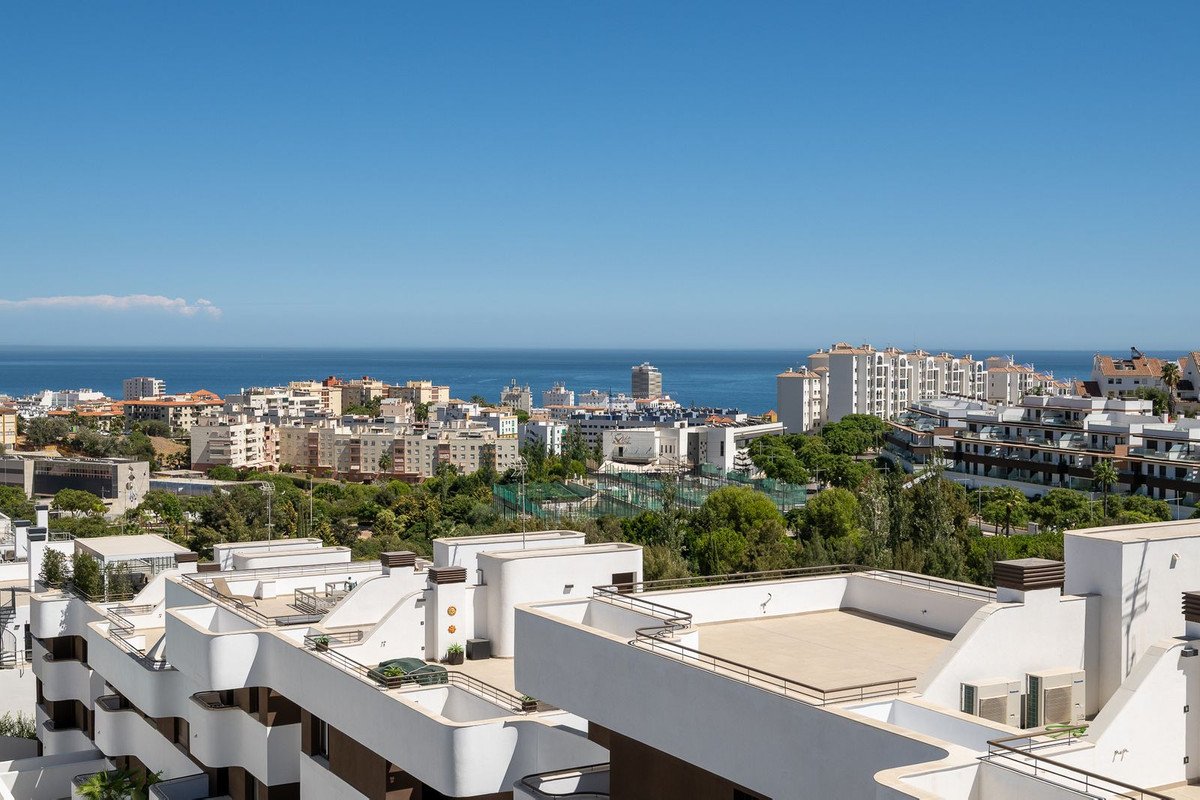 A wide view of an urban area with buildings and the sea in the distance under a clear blue sky.