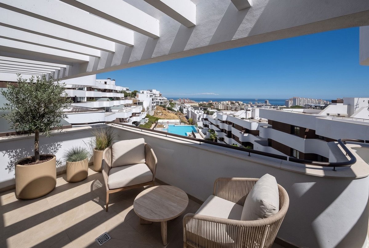 Terrace with two chairs and coffee table, overlooking a coastal town and the sea under a clear blue sky.