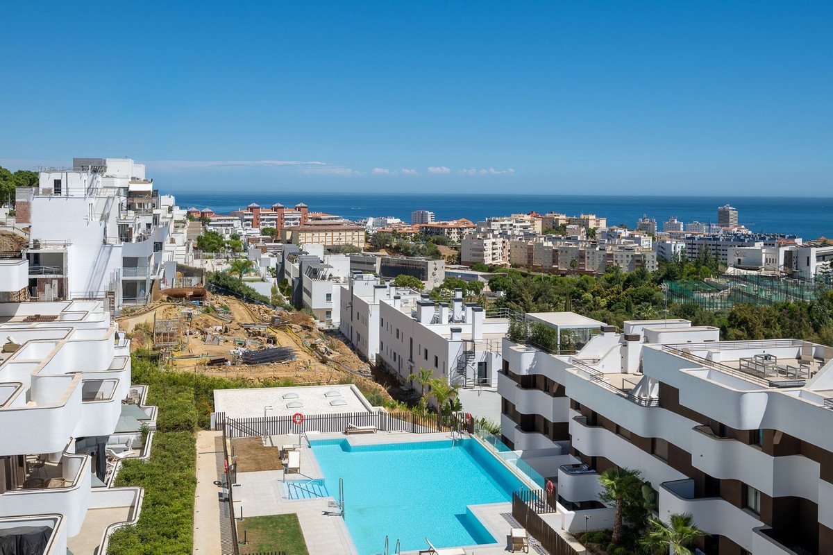 Modern apartments with a swimming pool and a view of the town and the sea under a clear blue sky.