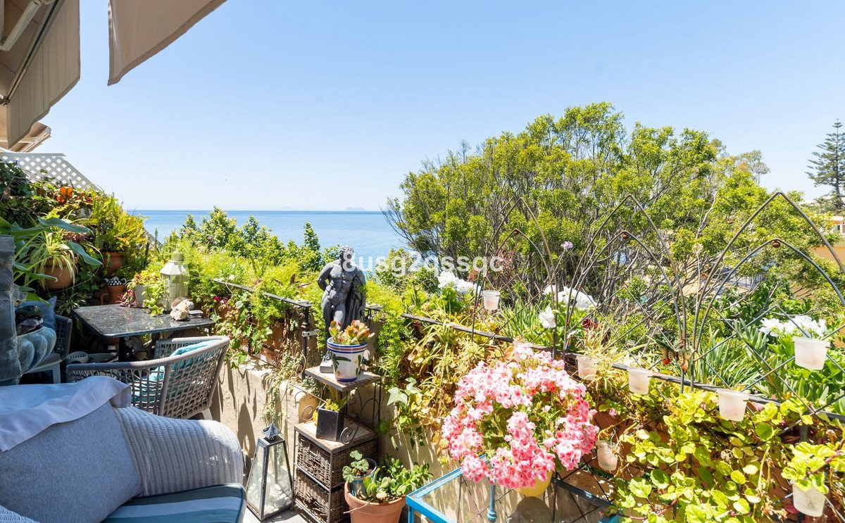 A lush balcony garden with seating and a beautiful view of the sea on a sunny day.