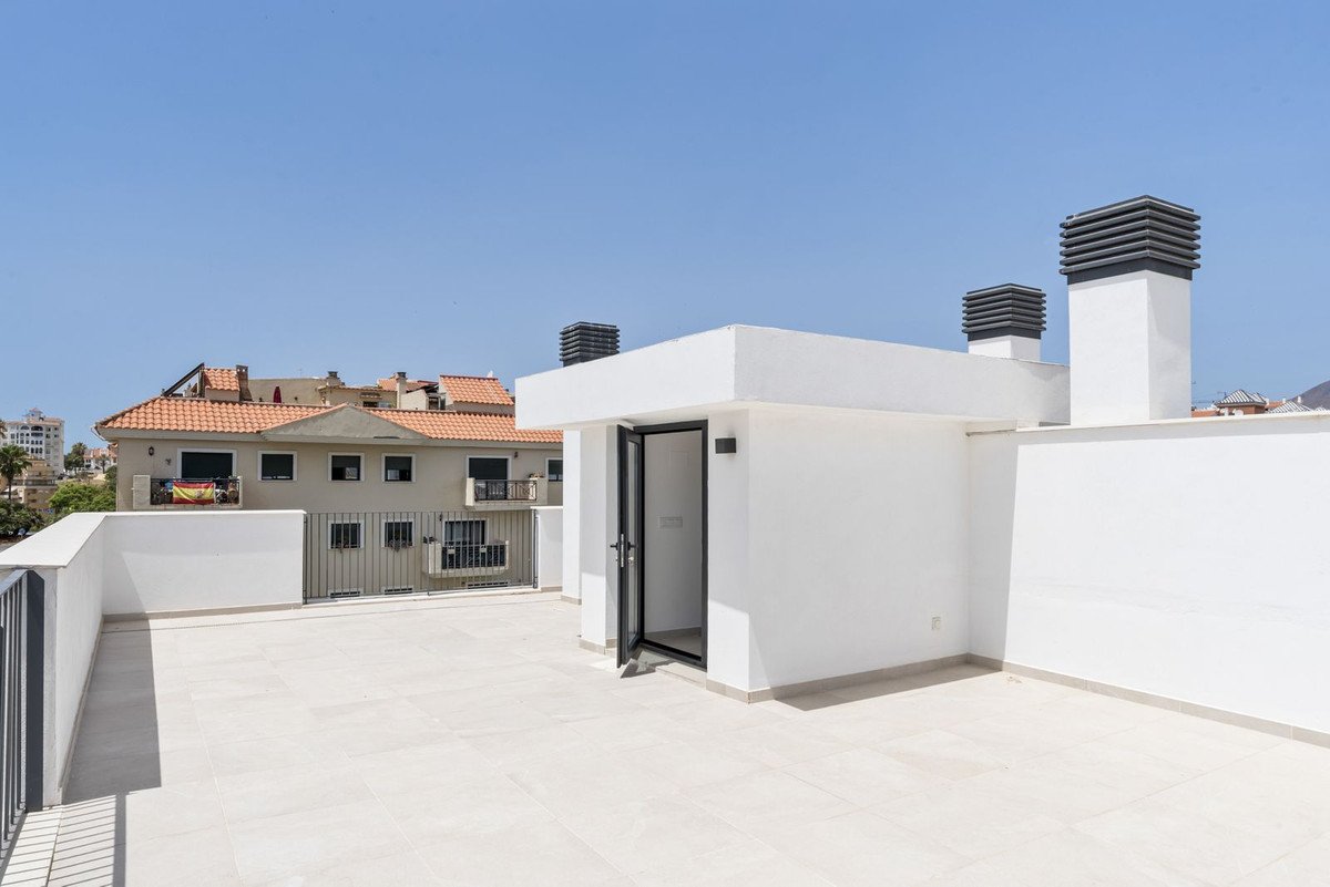Takterrass med vita plattor, glasdörr och ventilationsanläggning, med utsikt över bostadshus under klarblå himmel.