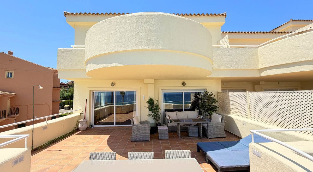 Spacious terrace with outdoor seating and dining furniture, overlooking the sea under a clear blue sky.