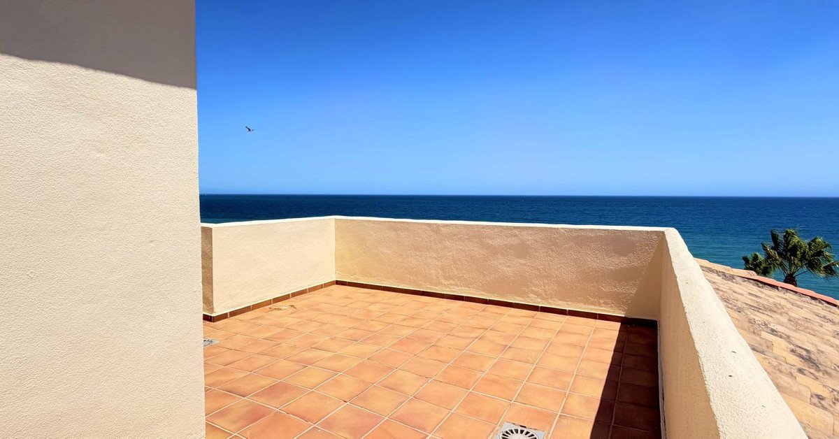 A spacious tiled terrace with a low wall, offering a clear view of the deep blue sea and a bright sunny sky.