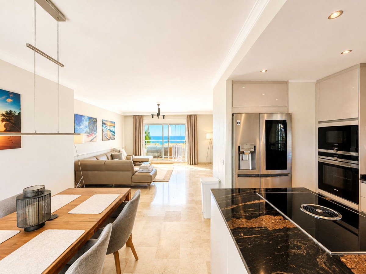 Modern living, dining, and kitchen area with a sofa, dining table, and island. Features a sea view through balcony doors.