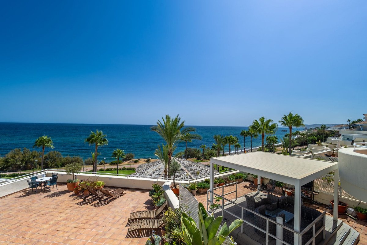 Spacious tiled terrace with outdoor furniture, lounge chairs, and palm trees, offering a stunning sea view under a clear blue sky.
