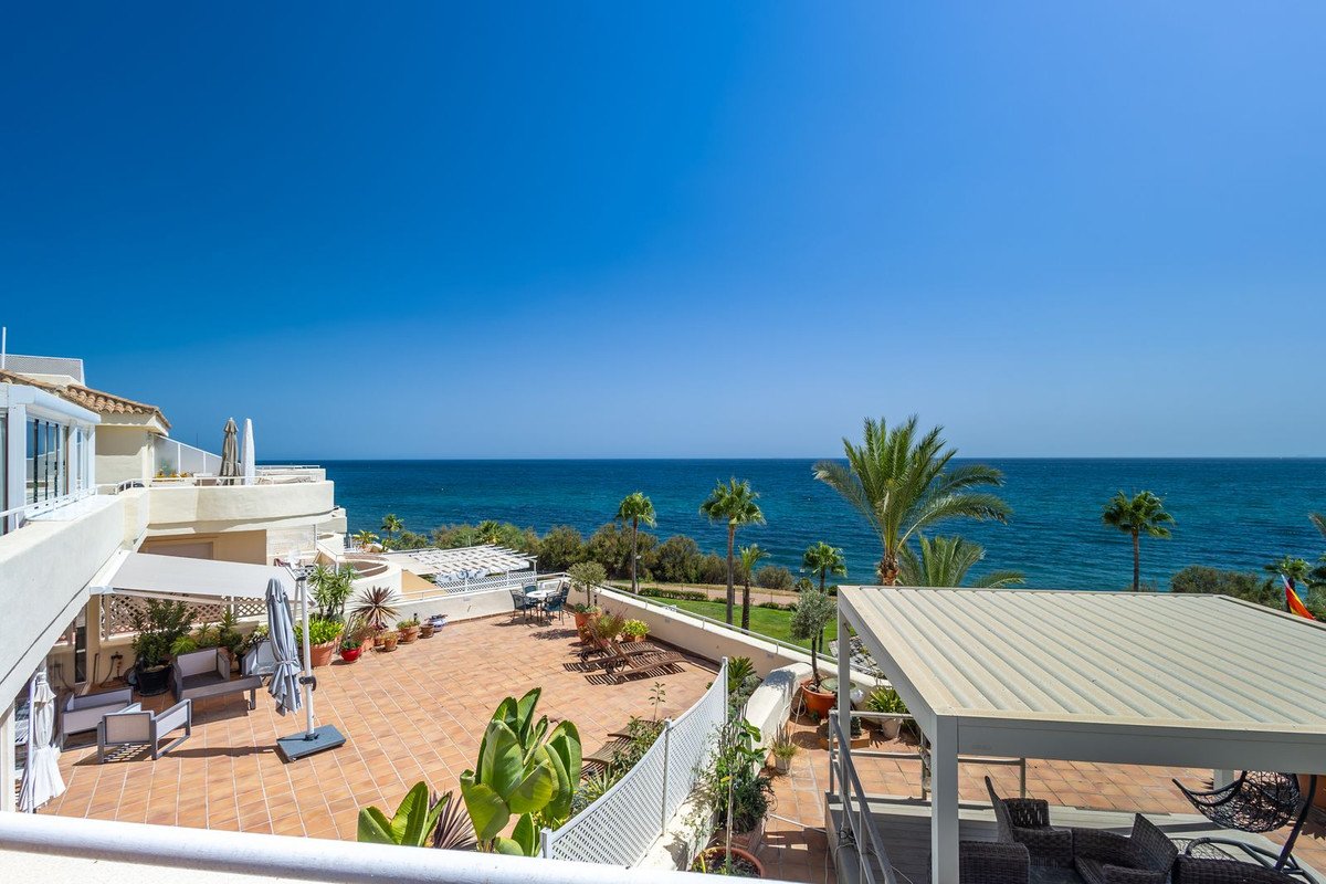 Spacious tiled terrace with outdoor seating, overlooking the turquoise sea and palm trees on a sunny day.