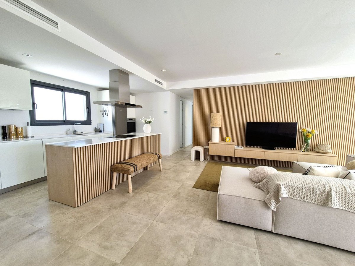A modern open-plan living area with a sleek kitchen, island, and a TV entertainment unit against a slatted wood wall.