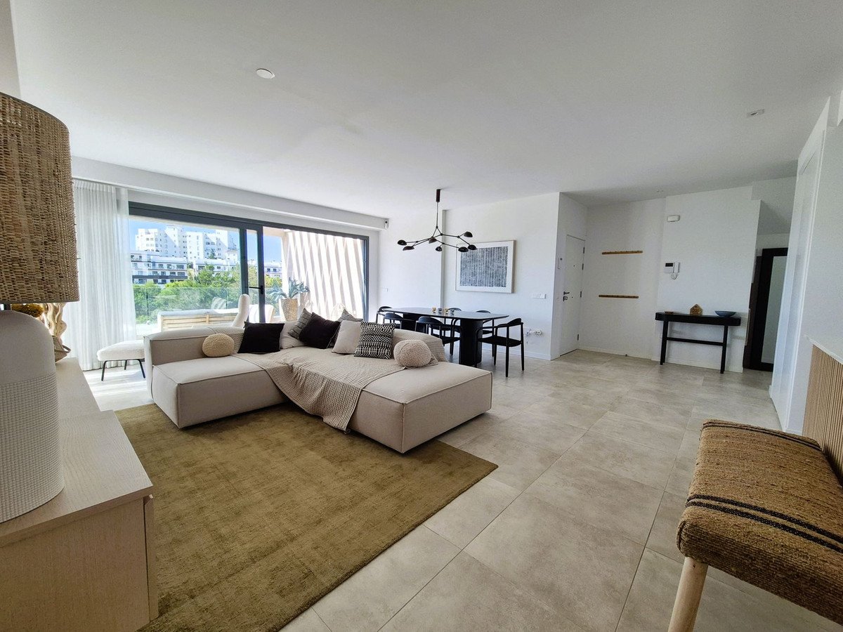 Spacious living and dining area with a large sectional sofa, modern dining table, and floor-to-ceiling windows offering city views.