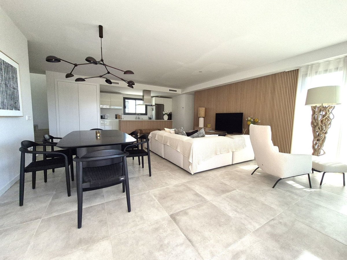 Modern living and dining area with open-plan kitchen, featuring a black table, white sofa, and wood-paneled wall.