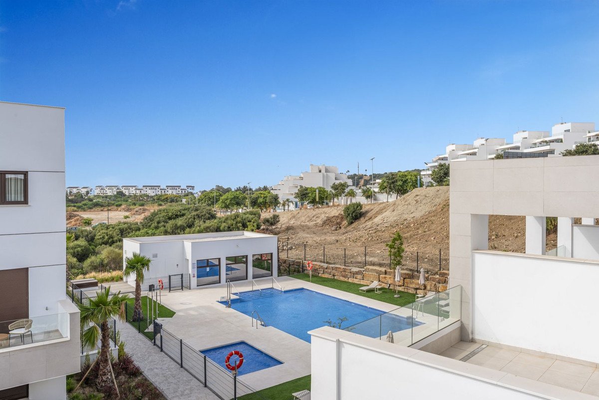 Modern apartment complex with swimming pool and sun loungers under a clear blue sky.