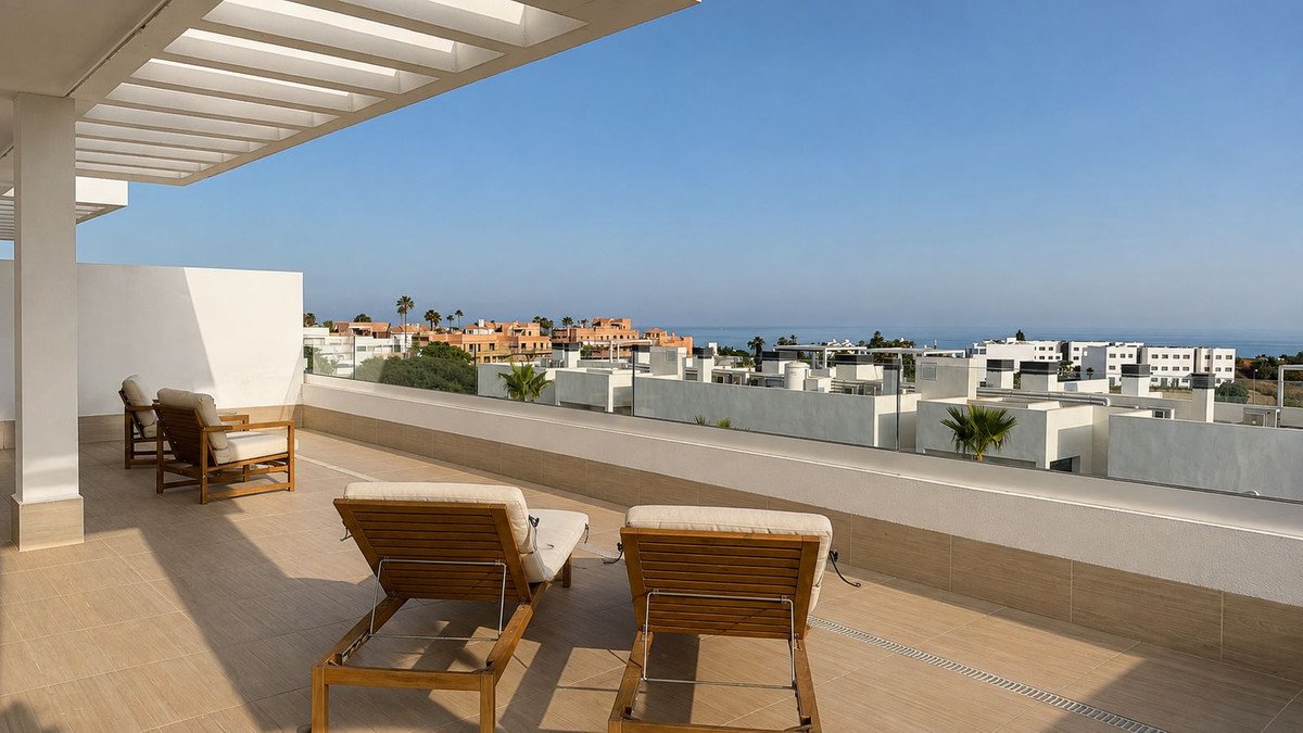 A sunny terrace with lounge chairs and a view of buildings and the sea.