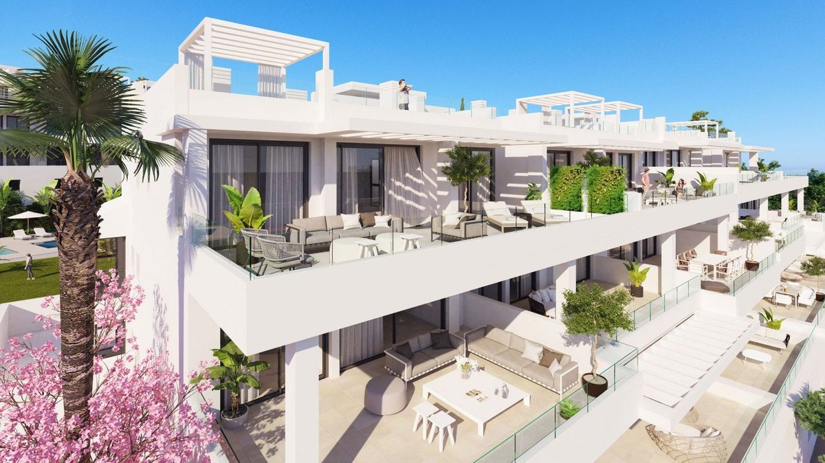 Modern apartments with spacious terraces, outdoor lounge areas, and a glimpse of the sea in the background.