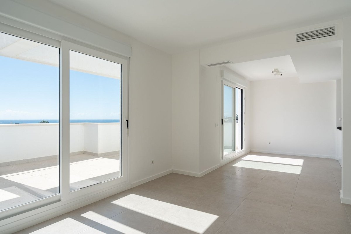 Bright living room with large windows overlooking a balcony and the sea. Modern interior with white walls.