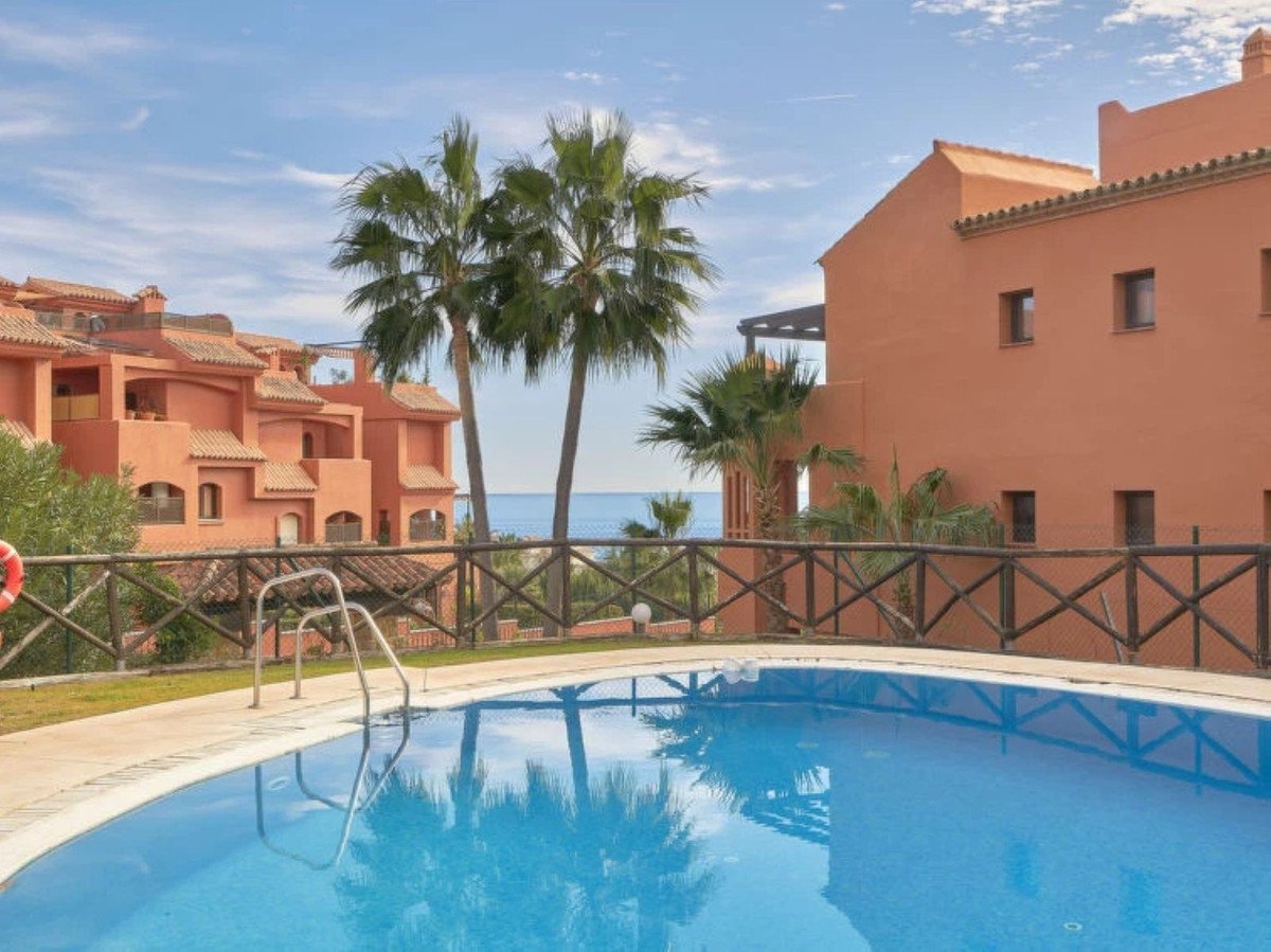 A swimming pool with palm trees and apartments in the background, overlooking the sea.